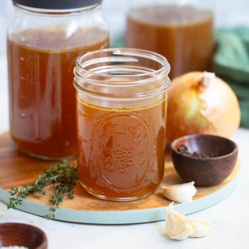 slow cooker chicken bone broth in clear mason jars on kitchen counter with decorative ingredients