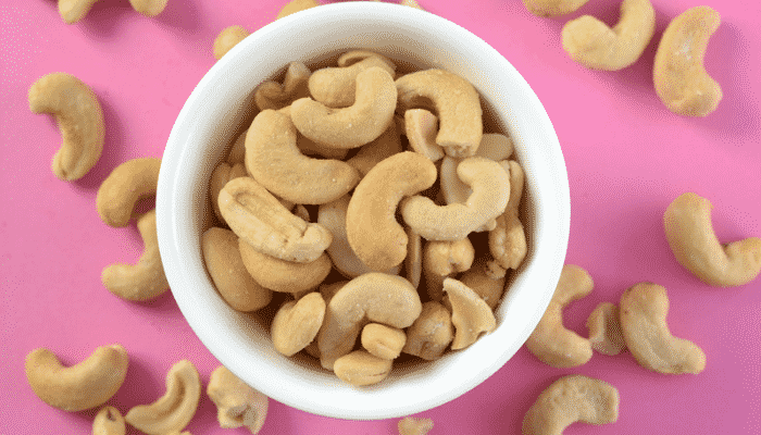 White bowl of cashew on a pink background