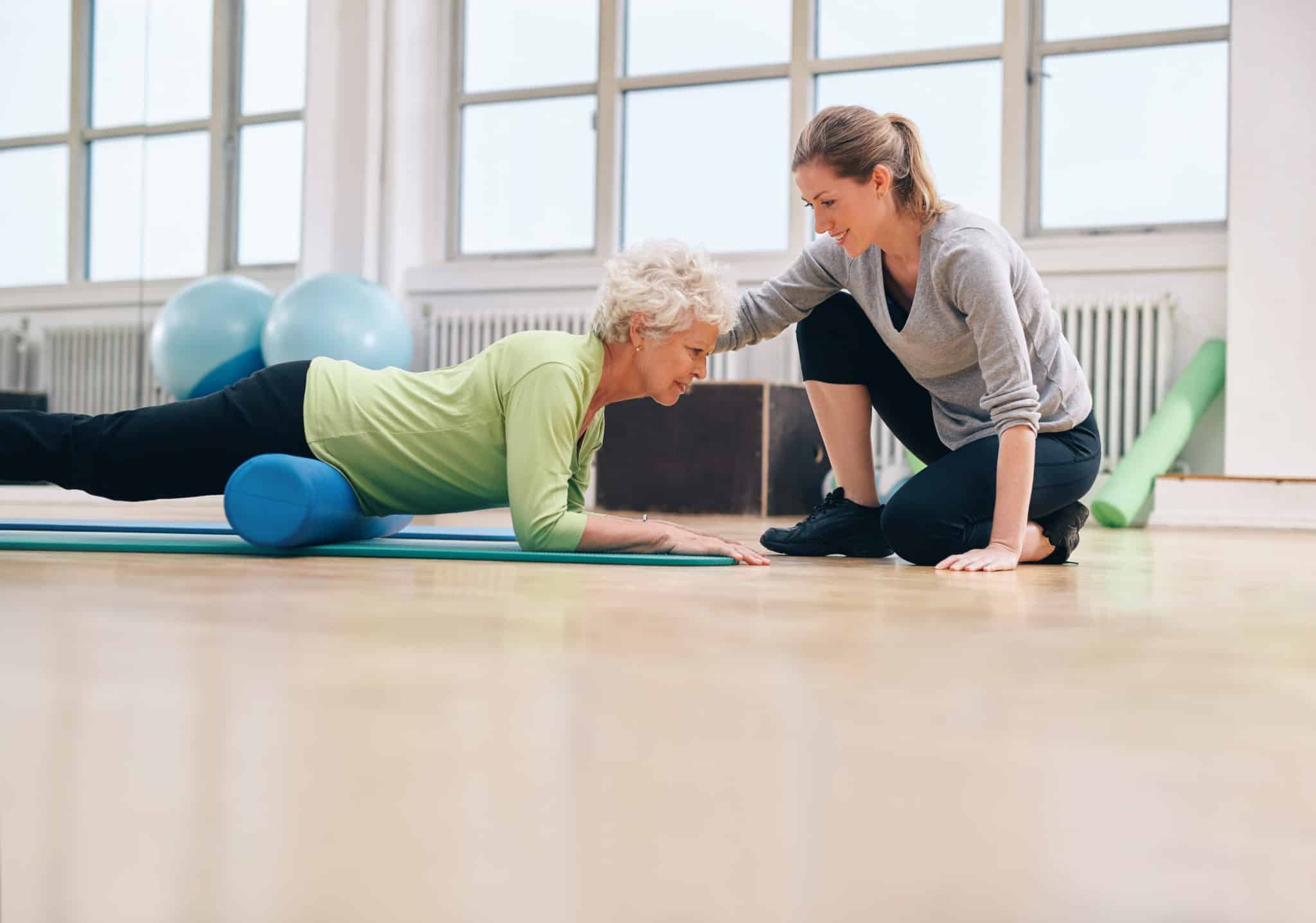 Middle aged woman using foam roller on thighs with help from young woman