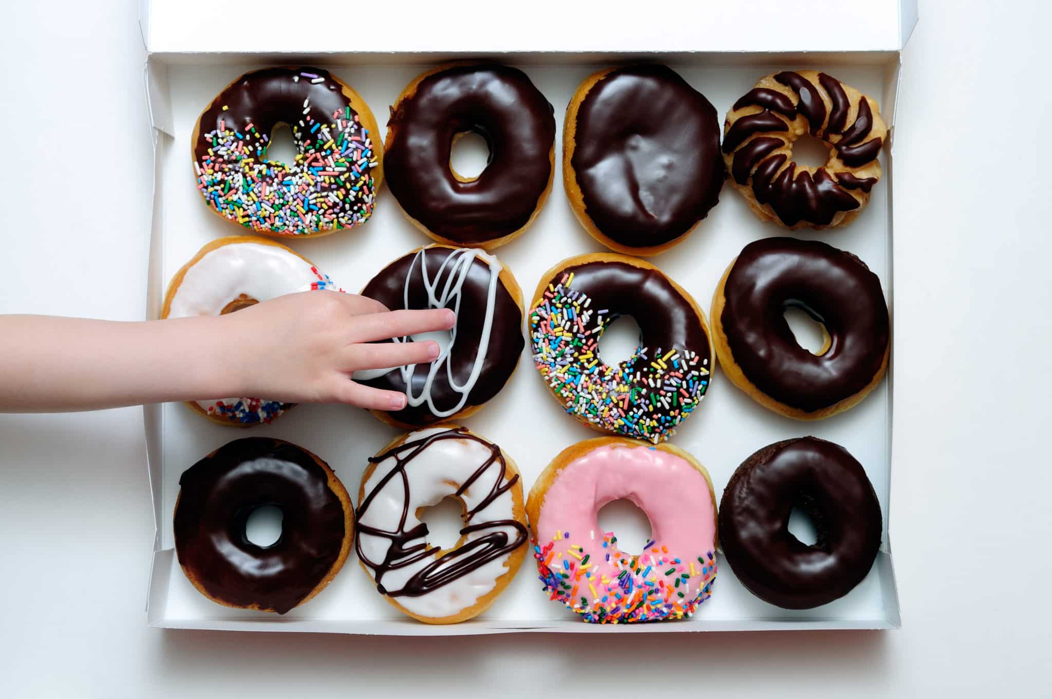 A hand reaching into a box of a dozen donuts.