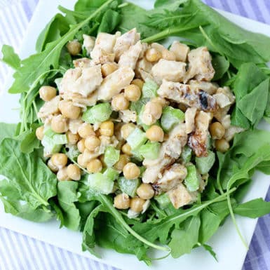 Arugula and spinach salad on white plate topped with creamy chicken salad and chickpeas