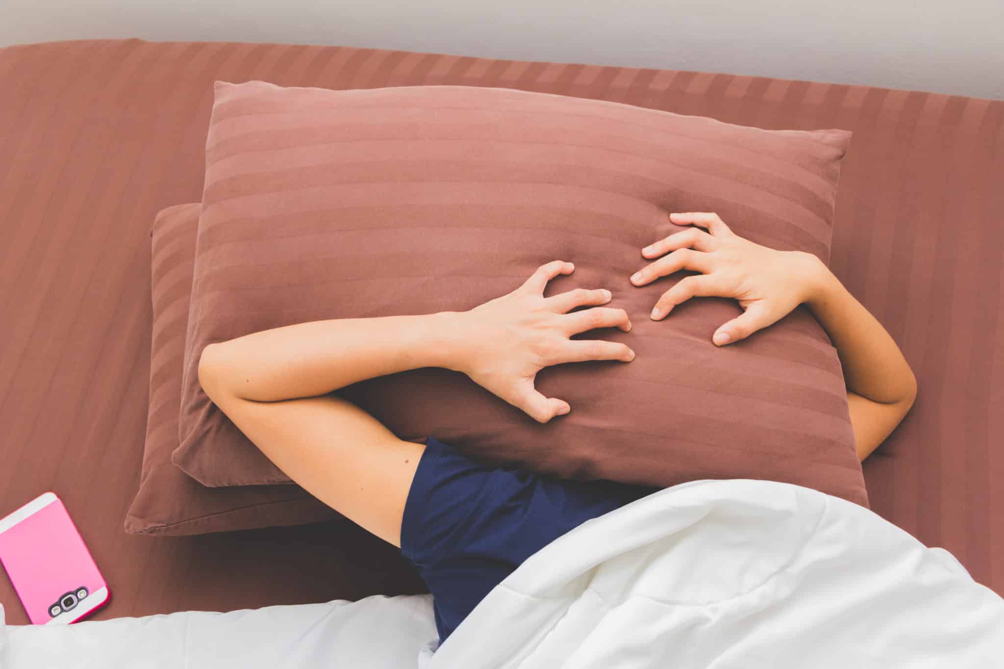A person struggling to sleep putting a pillow over their head in bed.