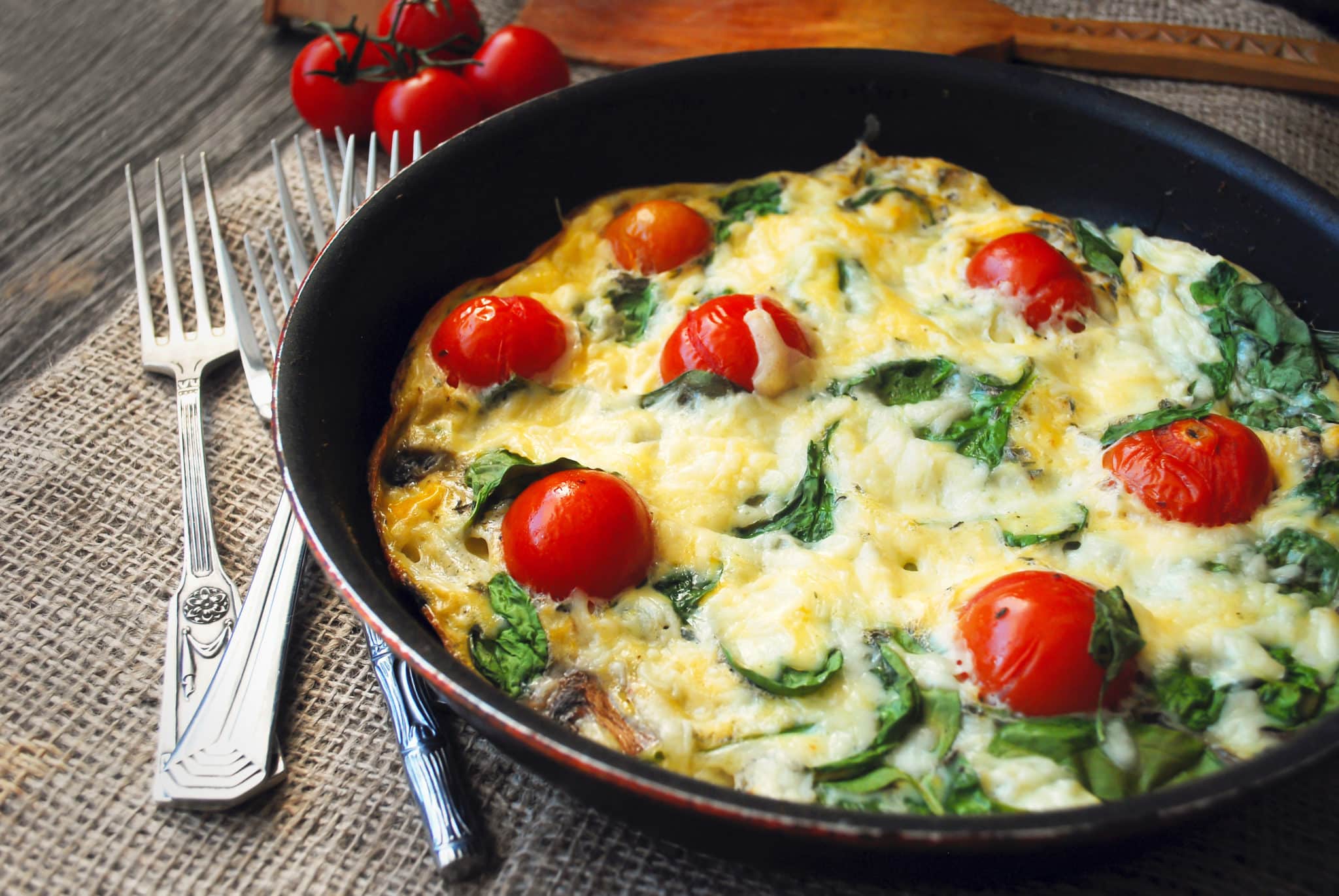 Frittata (italian omelet) with cherry tomatoes and spinach in pan on linen cloth.