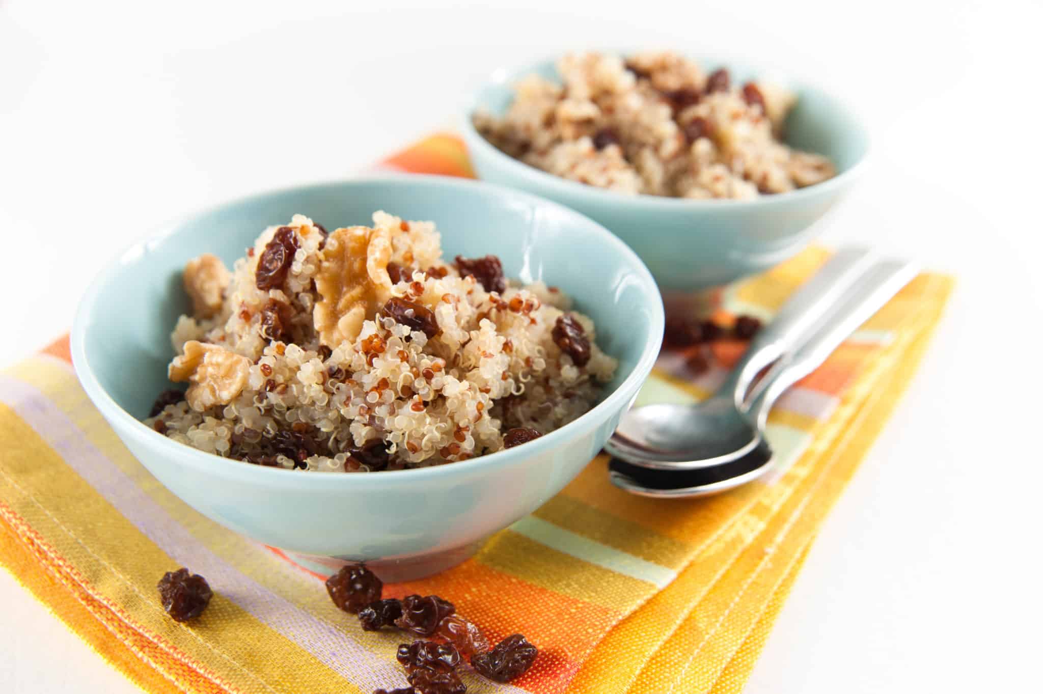 Healthy Quinoa Hot Cereal for Breakfast Served with Raisins and Walnuts in blue bowl next to spoons.