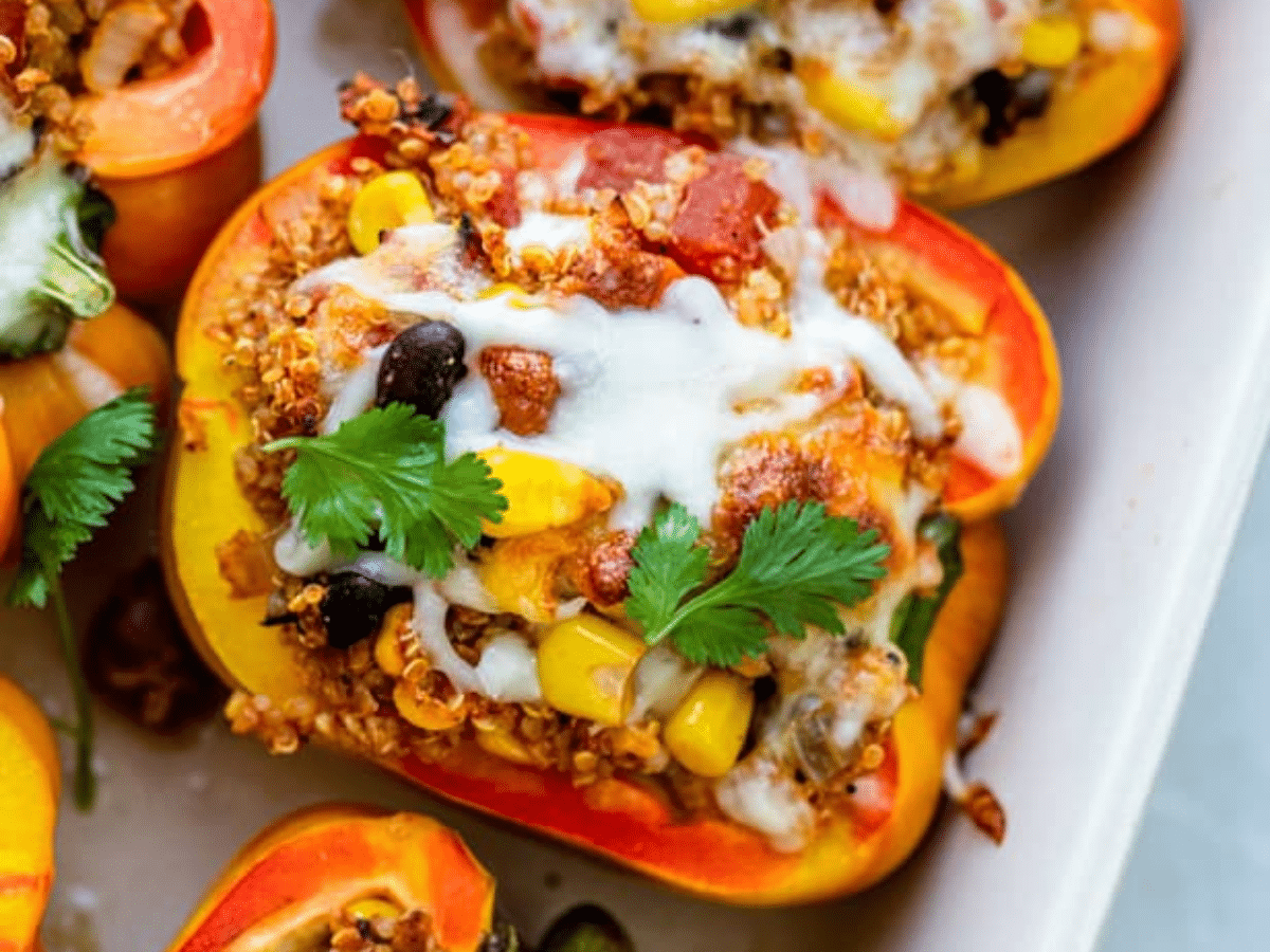 A close-up of quinoa stuffed red and yellow bell peppers topped with cheese, corn, beans, and fresh cilantro.