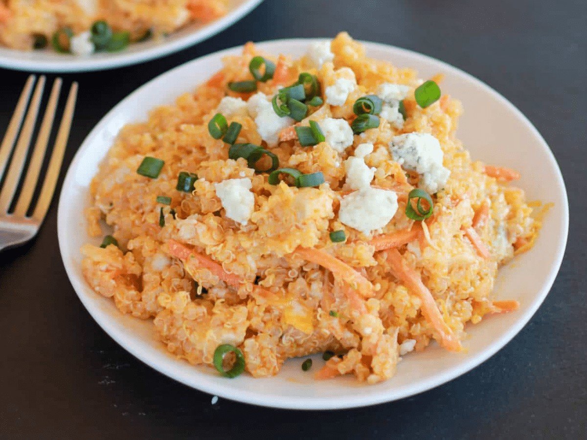 A plate of buffalo chicken quinoa salad topped with green onions, shredded carrots, and bleu cheese crumbles.