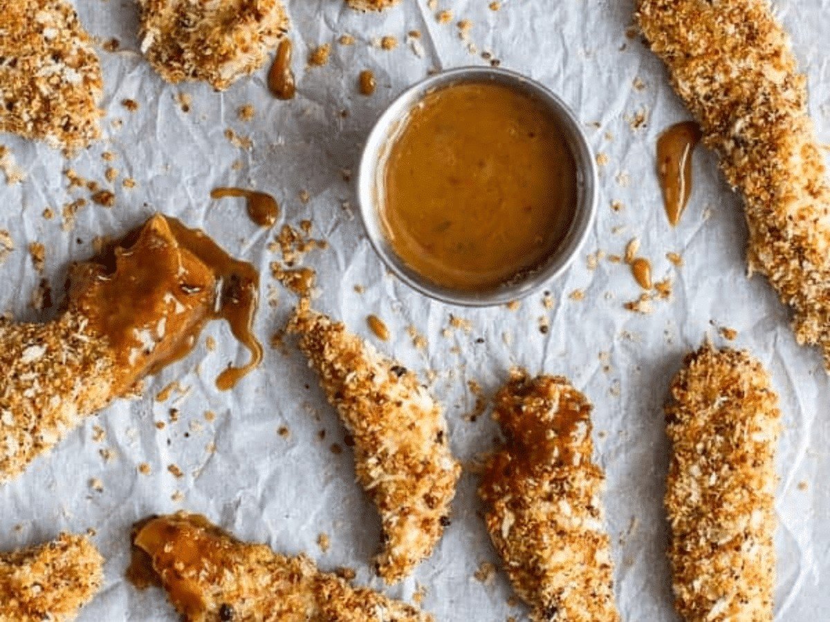 A bird's-eye view of the quinoa-crusted chicken strips next to a ramekin of BBQ honey mustard.