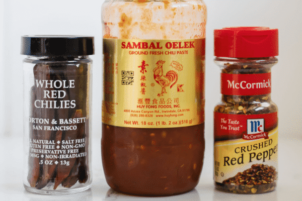 Whole red chiles, Sambal Oelek and crushed red pepper flakes lined up on a white background