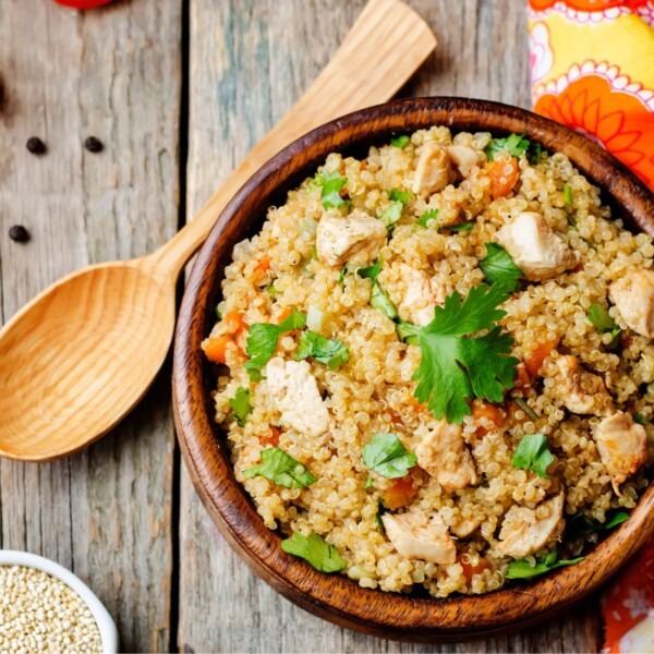 Bowl of Quinoa on a wooden table, with a wooden spoon next to the quinoa bowl/