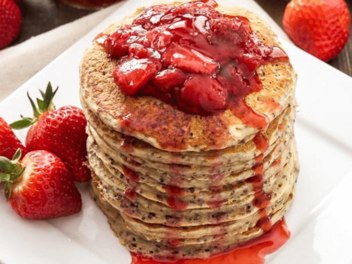 A stack of strawberry quinoa pancakes topped with fresh strawberries and a strawberrry jam.