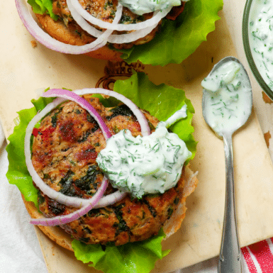An open-face healthy ground turkey burger recipe with yogurt sauce and red onion on a wood cutting board