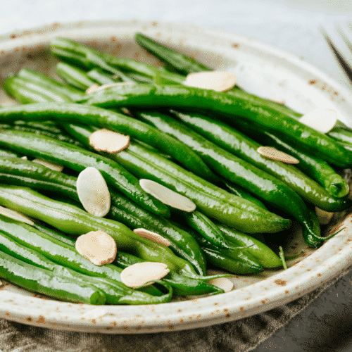 Roasted green beans with sliced almonds on a white plate