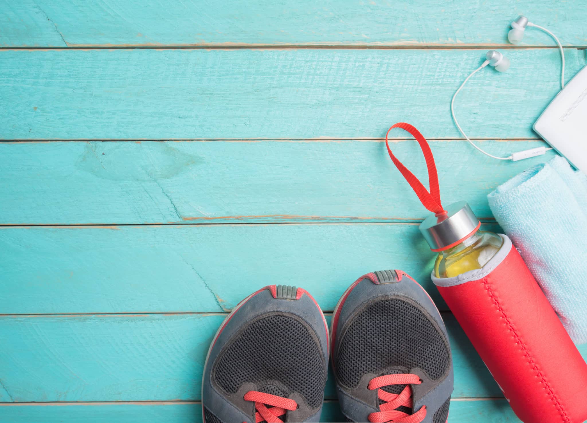 A pair of running shoes next to a water bottle against a wooden blue background.