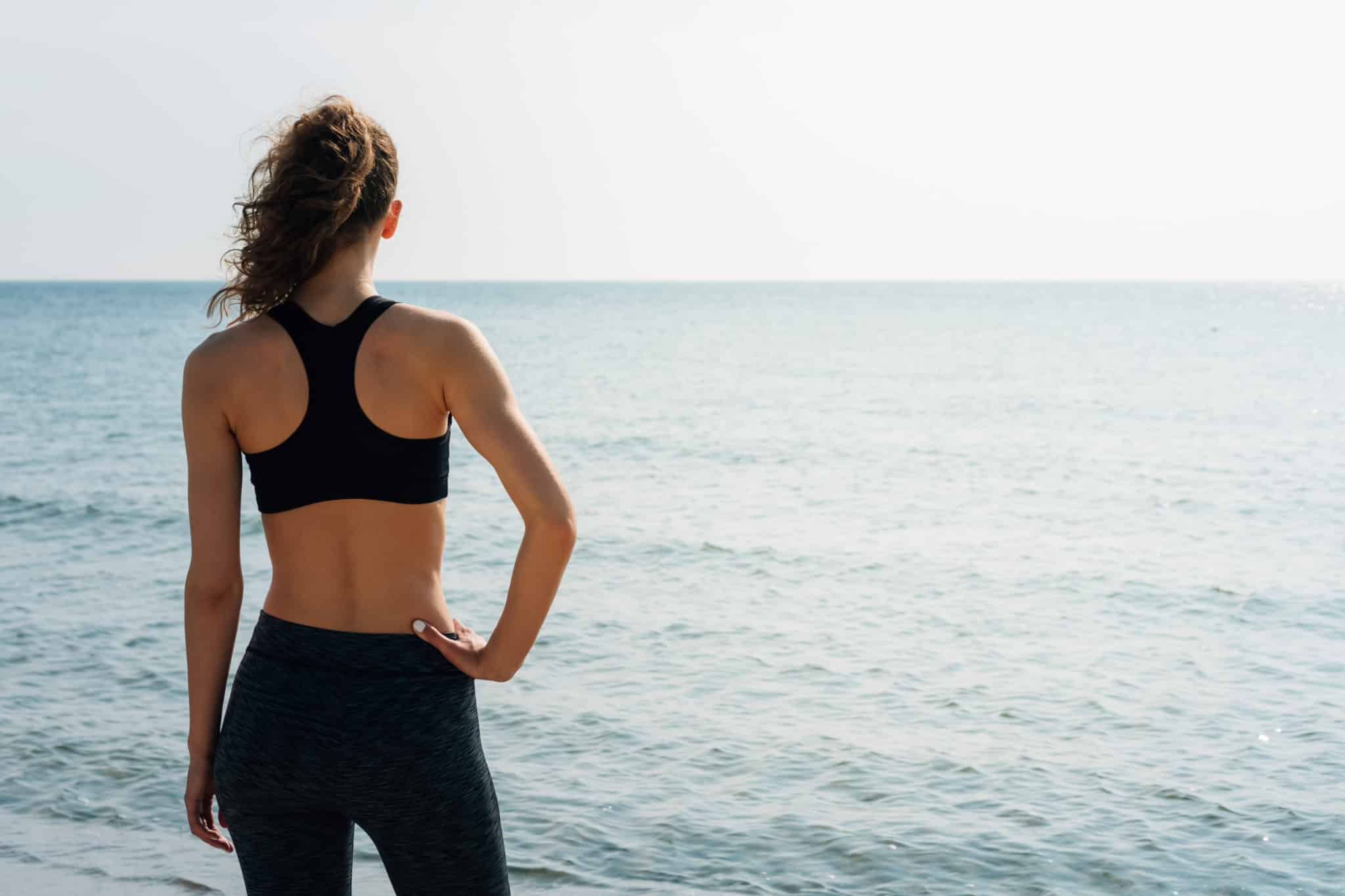 Woman standing in sports bra and leggings looking out into water