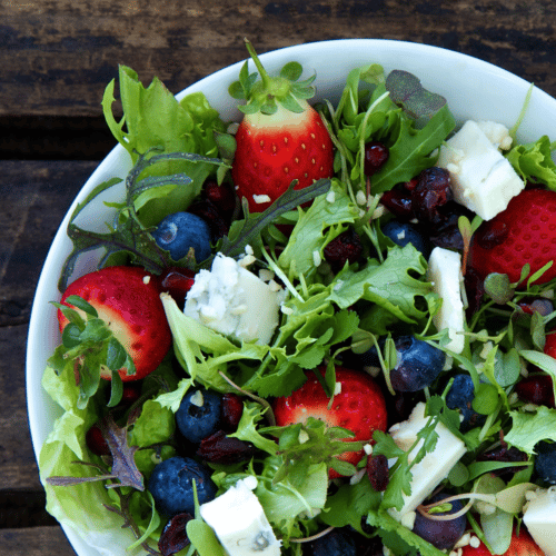 Arugula salad with berries in a white bowl