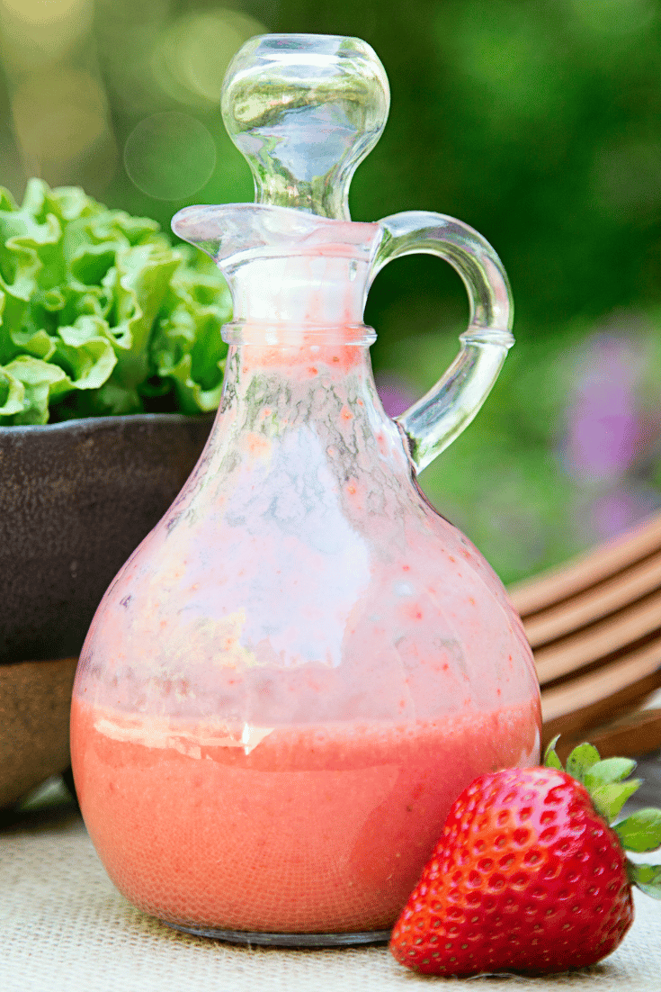 Strawberry vinaigrette in a glass jar with a strawberry on the foreground and greens in the background