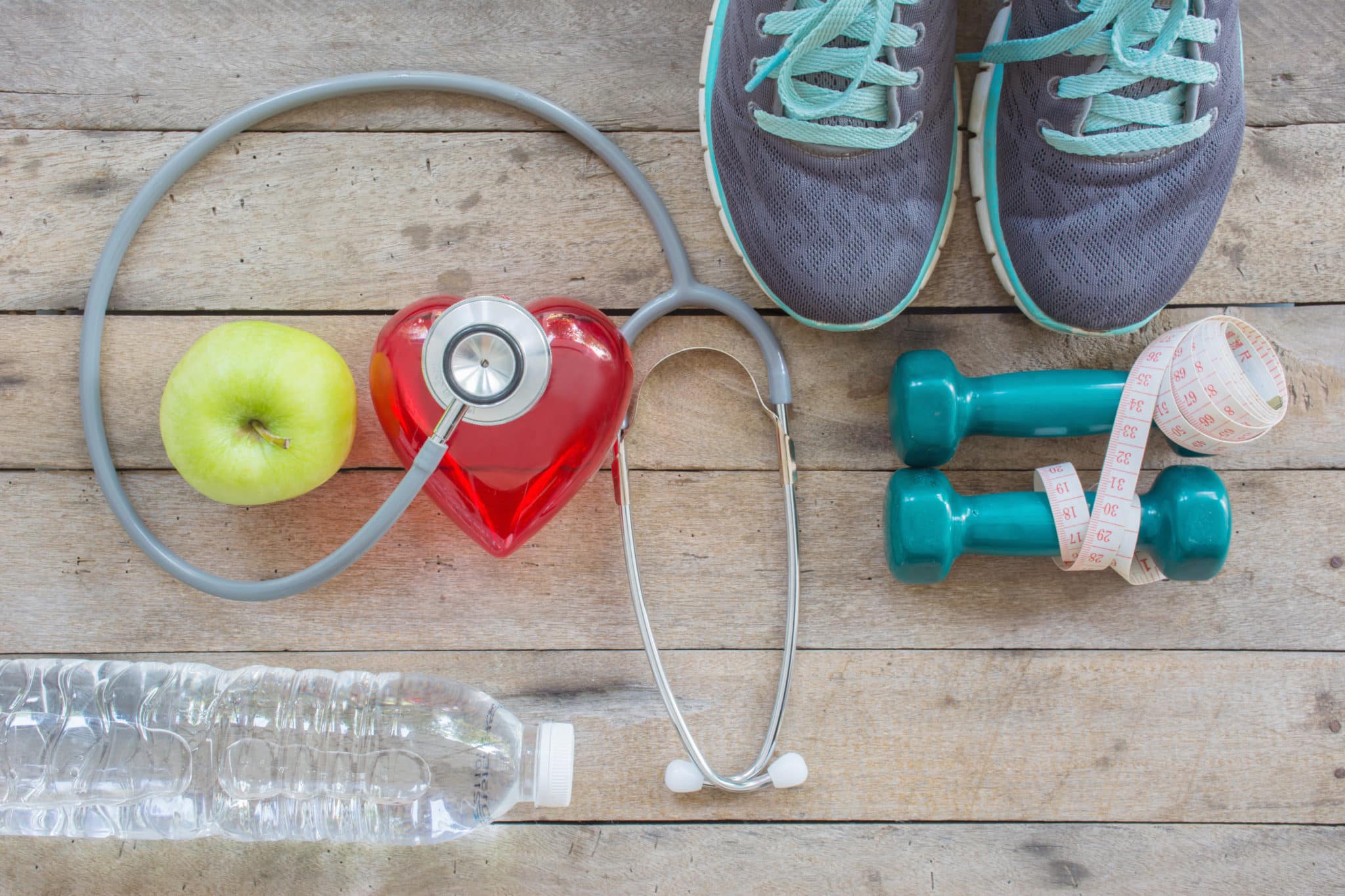 Tennis shoes, dumbbells, water bottle, apple and stethoscope all sitting together on wood planks