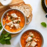 two bowls of tuscan tomato soup with garnish on white countertop background