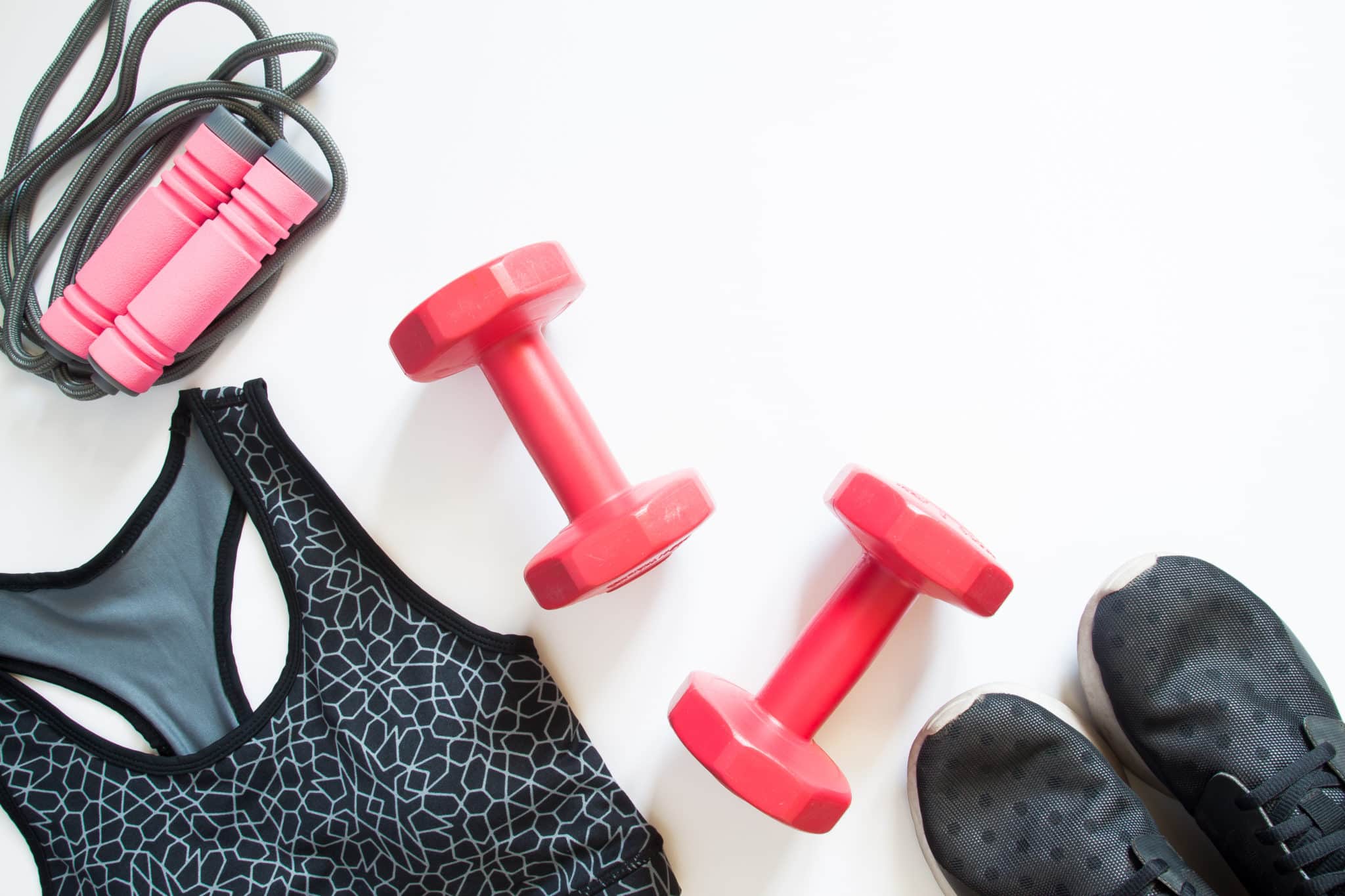 A pair of small pink dumbbells next to a sports bra and shoes.