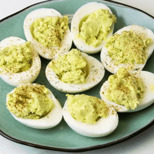 Avocado deviled eggs sitting on blue plate sprinkled with dill and paprika