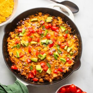 healthy chili cheese dip prepared sitting in pan on white counter with chips and lime slices in bowls