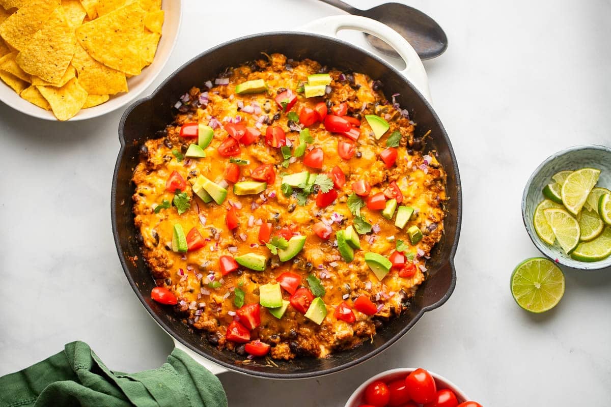 healthy chili cheese dip prepared sitting in pan on white counter with chips and lime slices in bowls