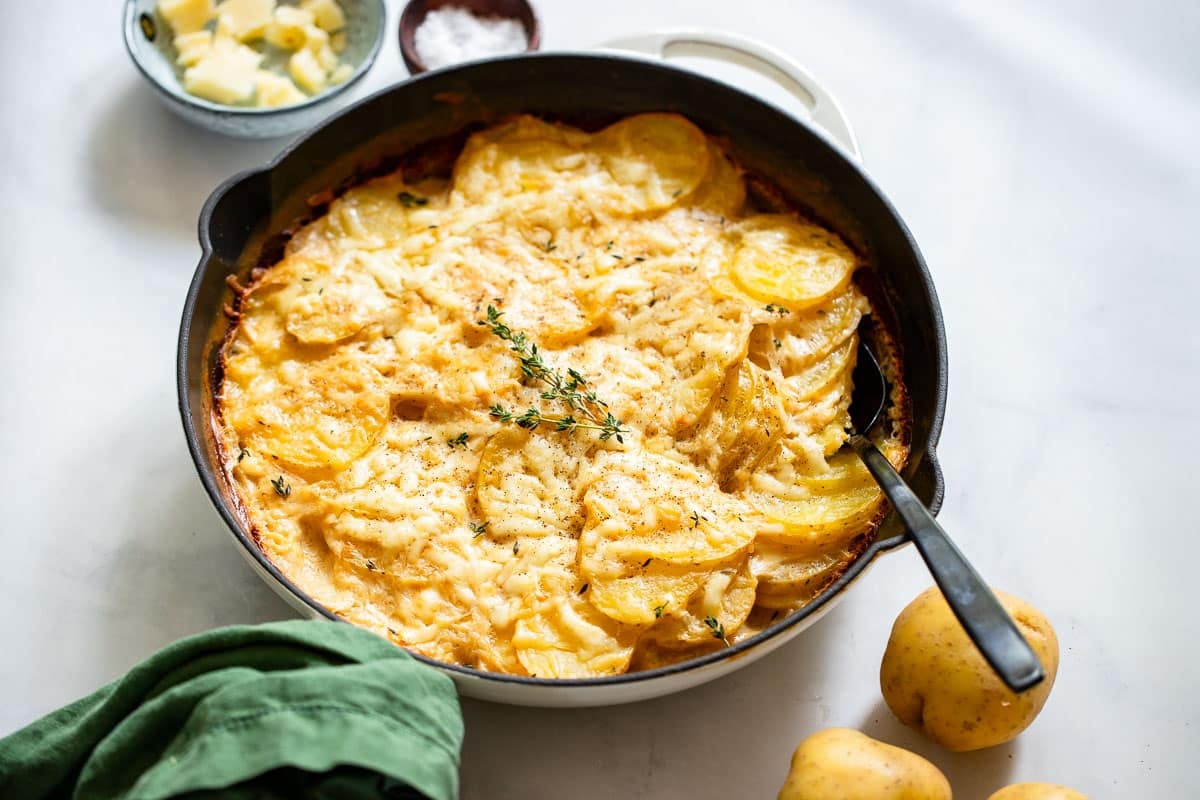 low fat scalloped potatoes in skillet with serving spoon on white counter