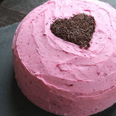 pink cake with pink heart on top sits on dark surface