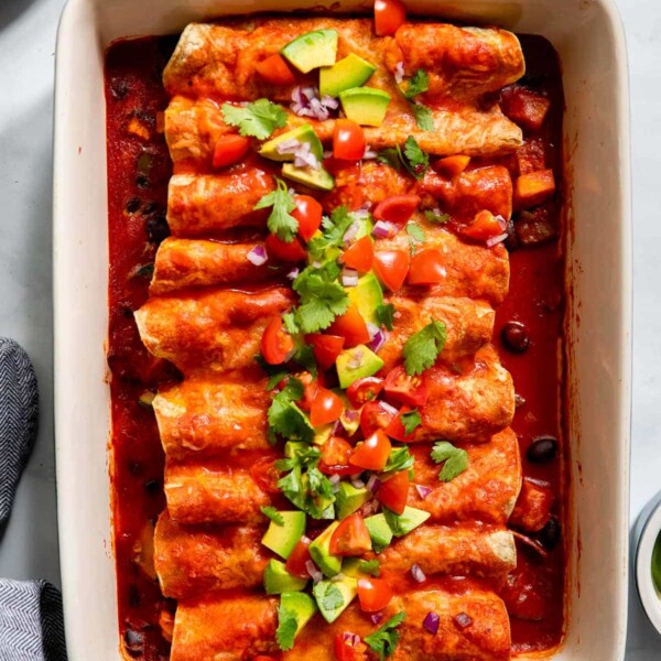 vegetarian black bean enchiladas topped with tomatoes and cilantro in a baking dish.