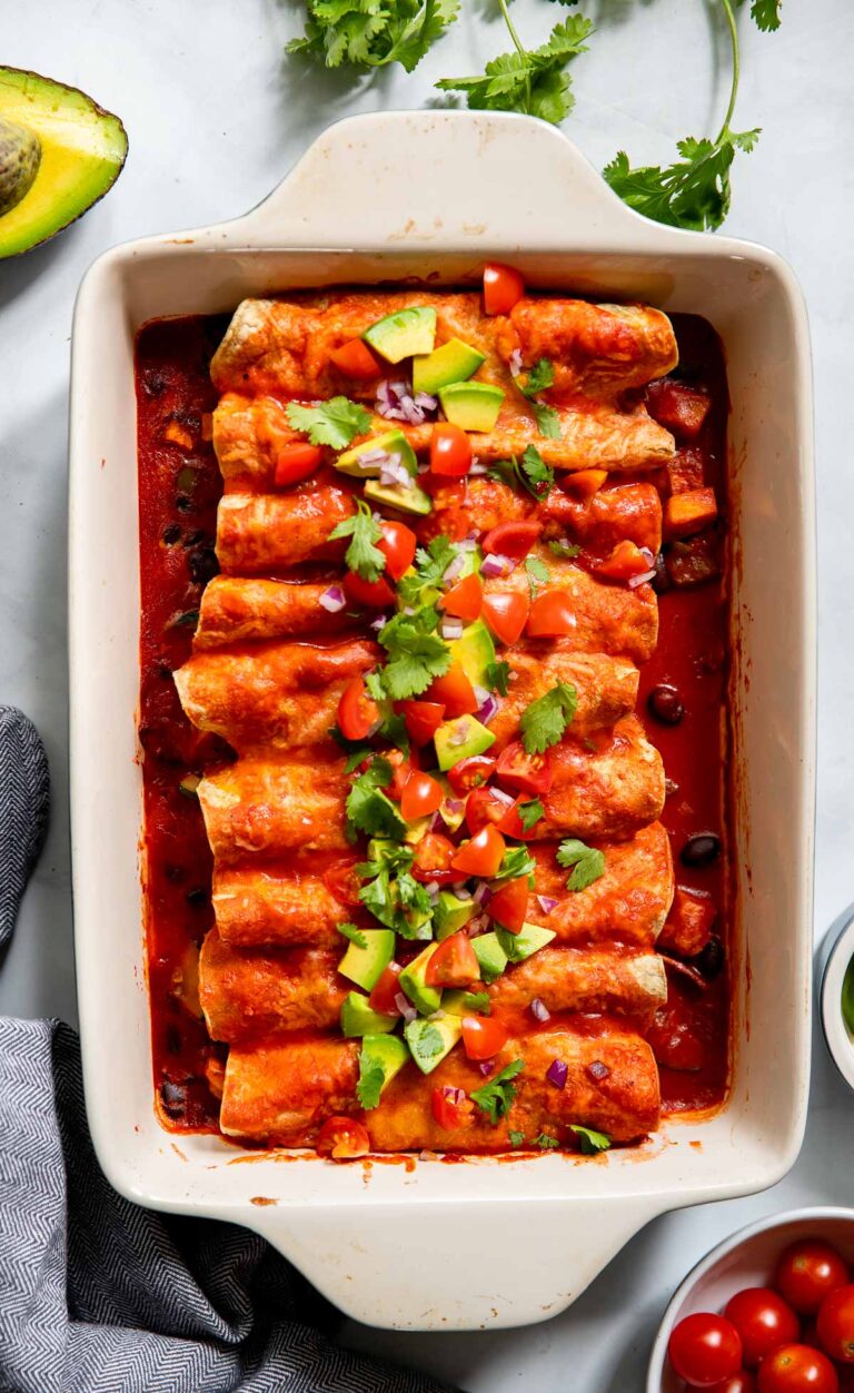 vegetarian black bean enchiladas topped with tomatoes and cilantro in a baking dish.