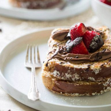 French toast on a plate with a fork and chocolate covered strawberries