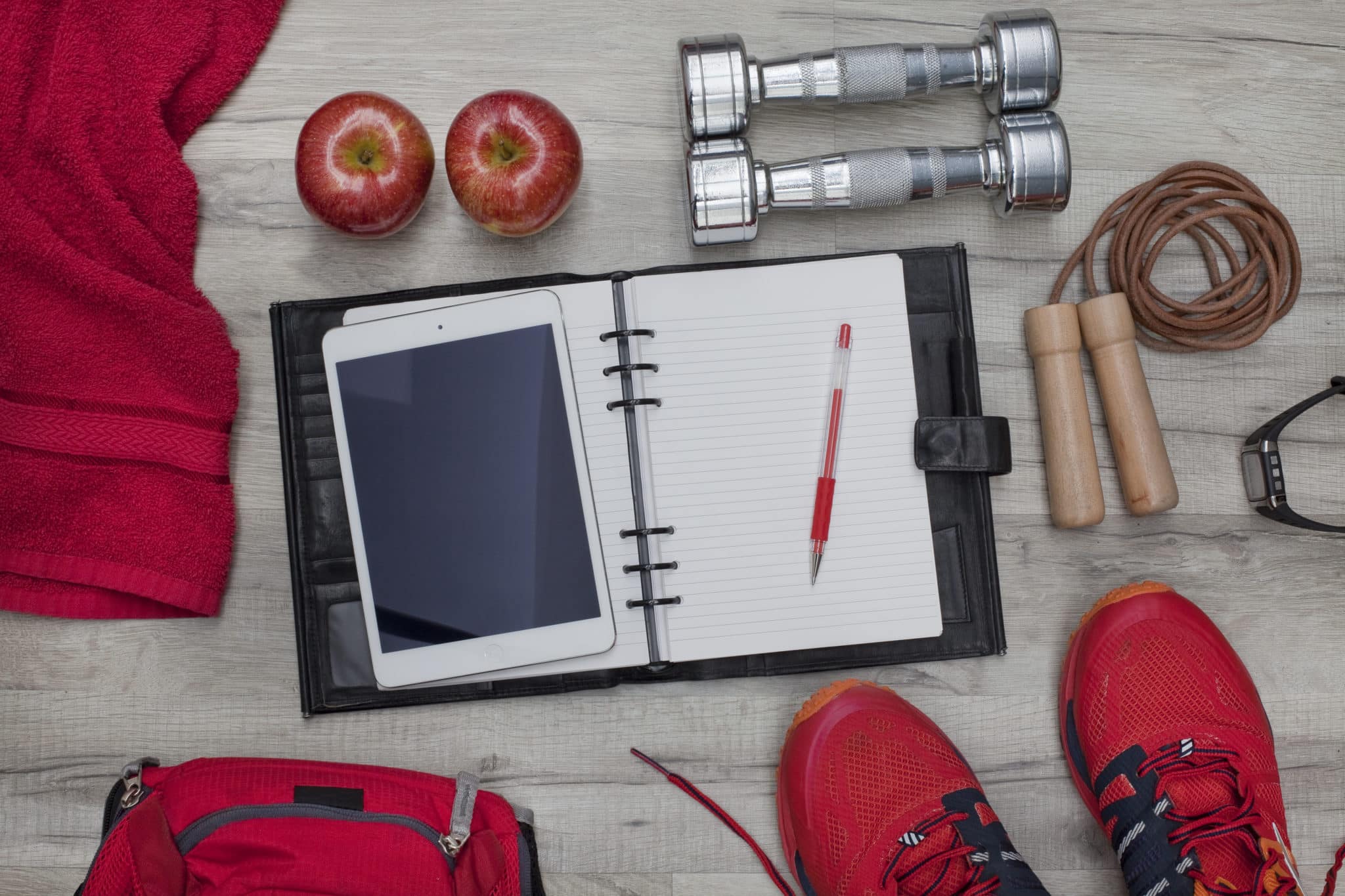 A notebook and ipad set up with dumbbells, apples, and tennis shoes