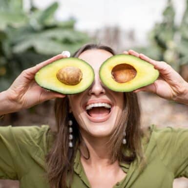 woman holding heart healthy fat avocados over eyes