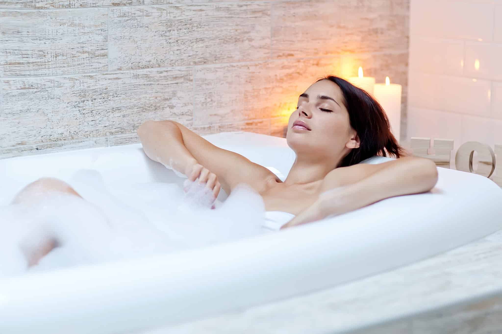 Woman lying in bubble bath with candles behind her