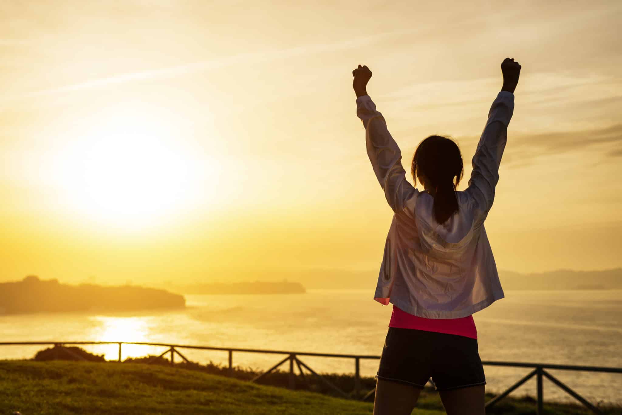 Woman with arms raised celebrating success with beautiful sunset