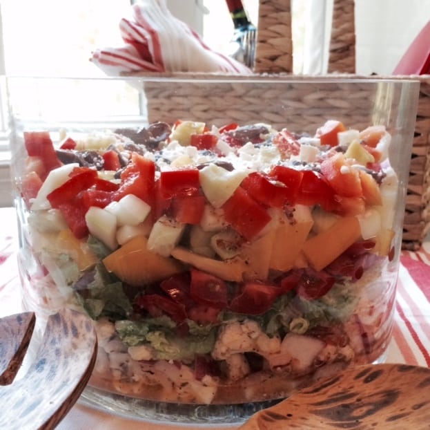 Greek layer salad with tomatoes, cauliflower, feta, olives, cucumber and romaine in glass trifle bowl