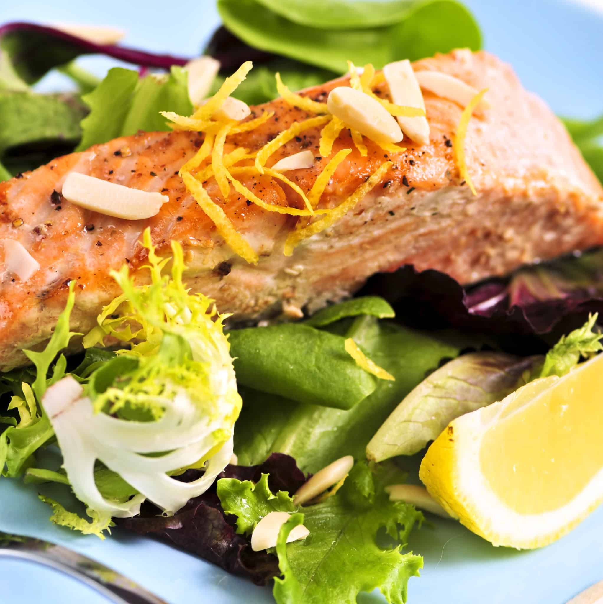 Grilled salmon on top of green lettuce, slivered almonds and lemon