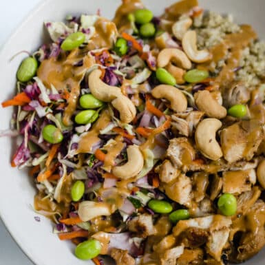 A gluten-free, dairy-free crunchy thai salad with quinoa and chicken in a bowl sprinkled with cashews and edamame