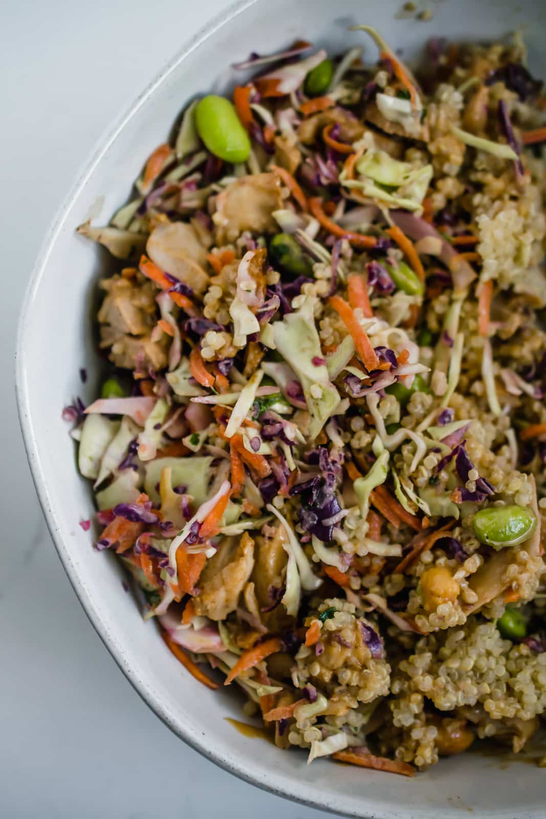 A gluten-free, dairy-free crunchy thai salad with quinoa and chicken in a bowl sprinkled with cashews and edamamev