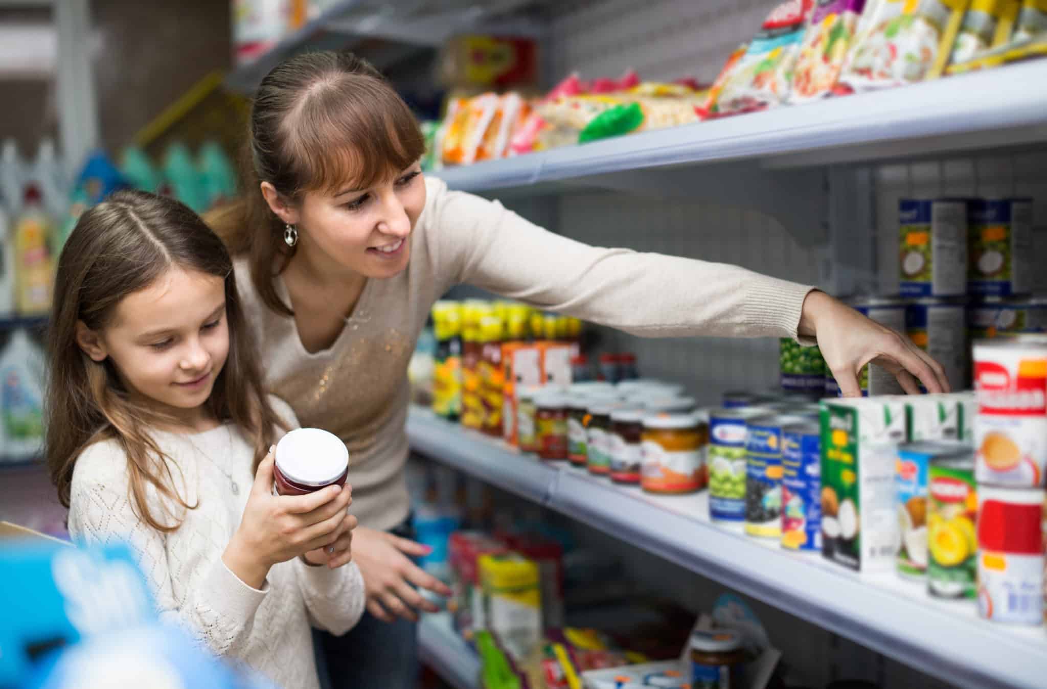Mom and daughter in grocery store reading labels on canned goods