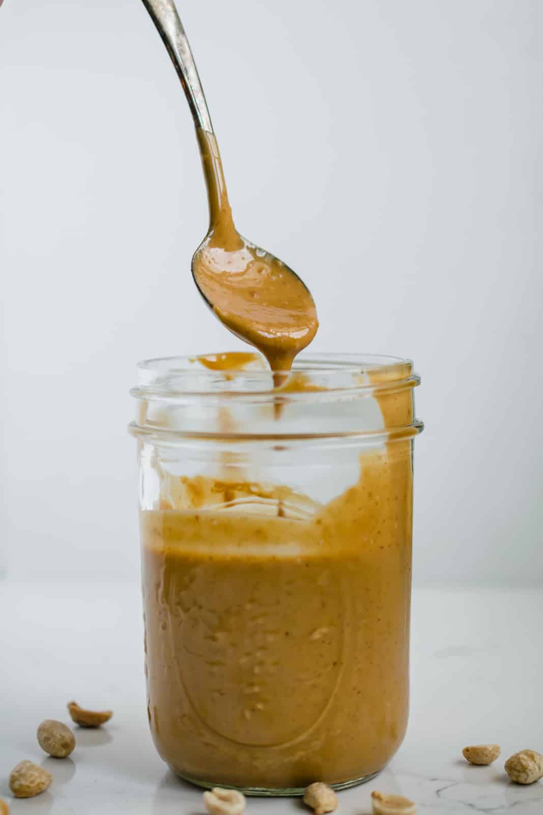 Mason jar of Thai peanut dressing with spoon hovering above and dripping sauce