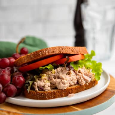 healthy tuna salad sandwich with tomato and lettuce on a plate with grapes.