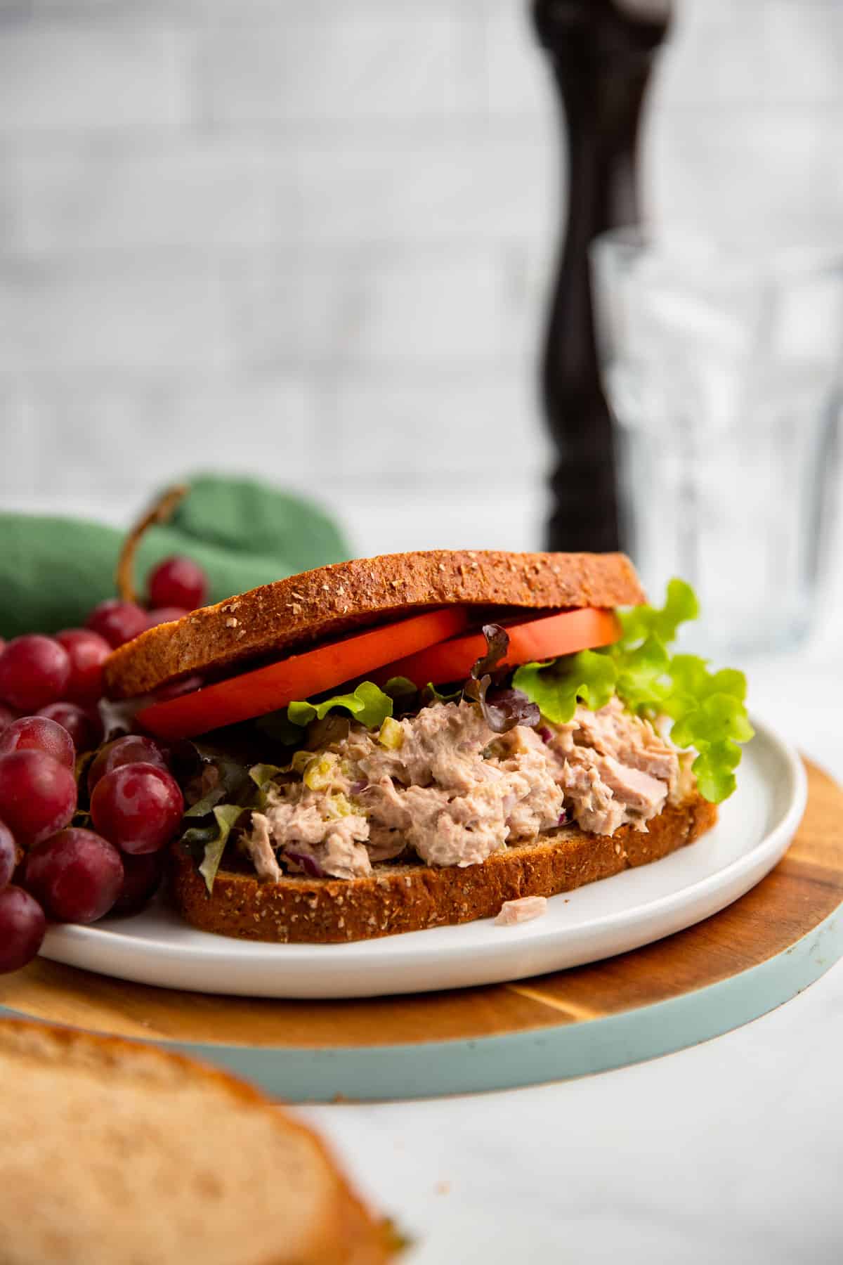 healthy tuna salad sandwich with tomato and lettuce on a plate with grapes.