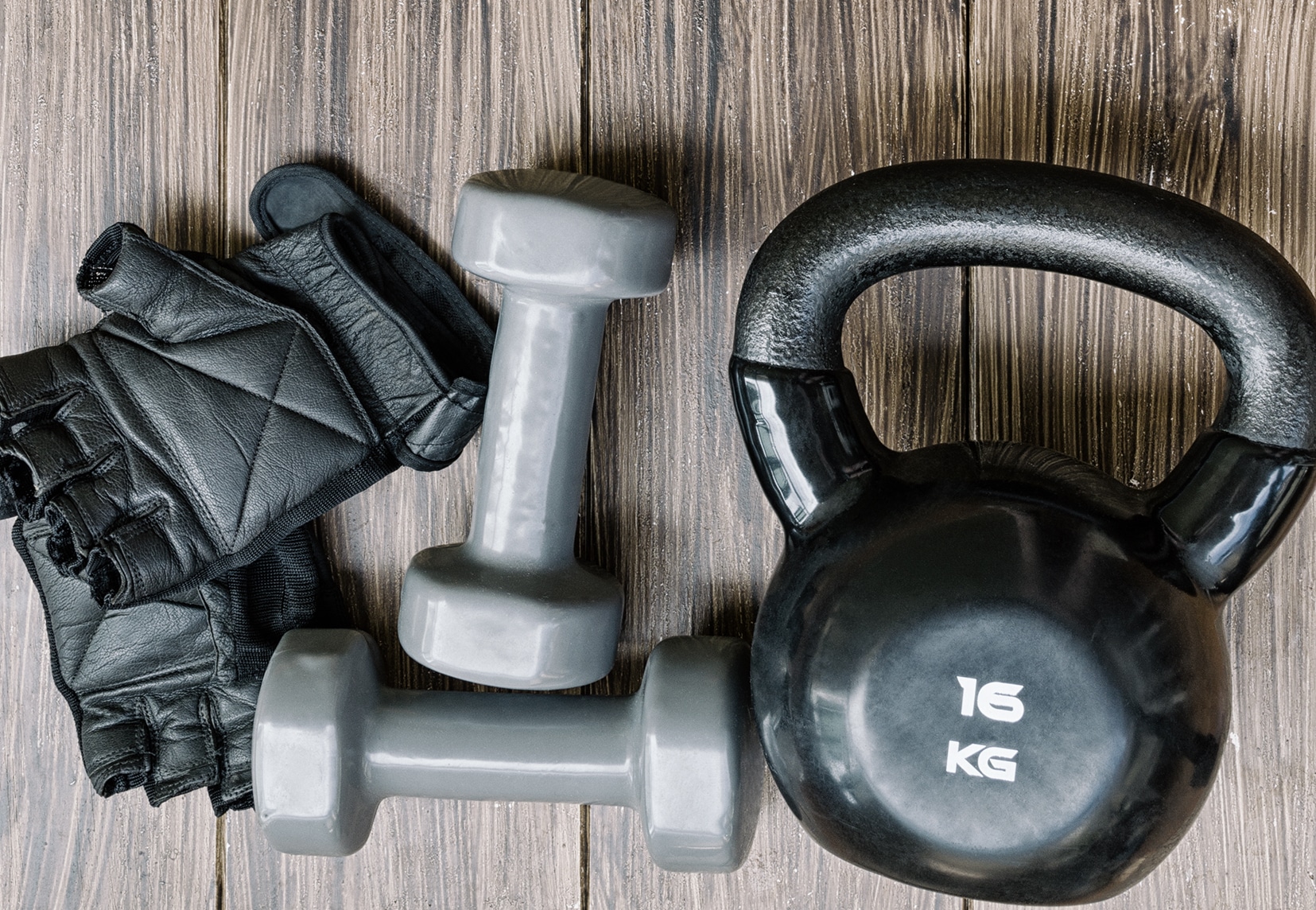 Gray dumbbells and black kettlebell with workout gloves on wood background