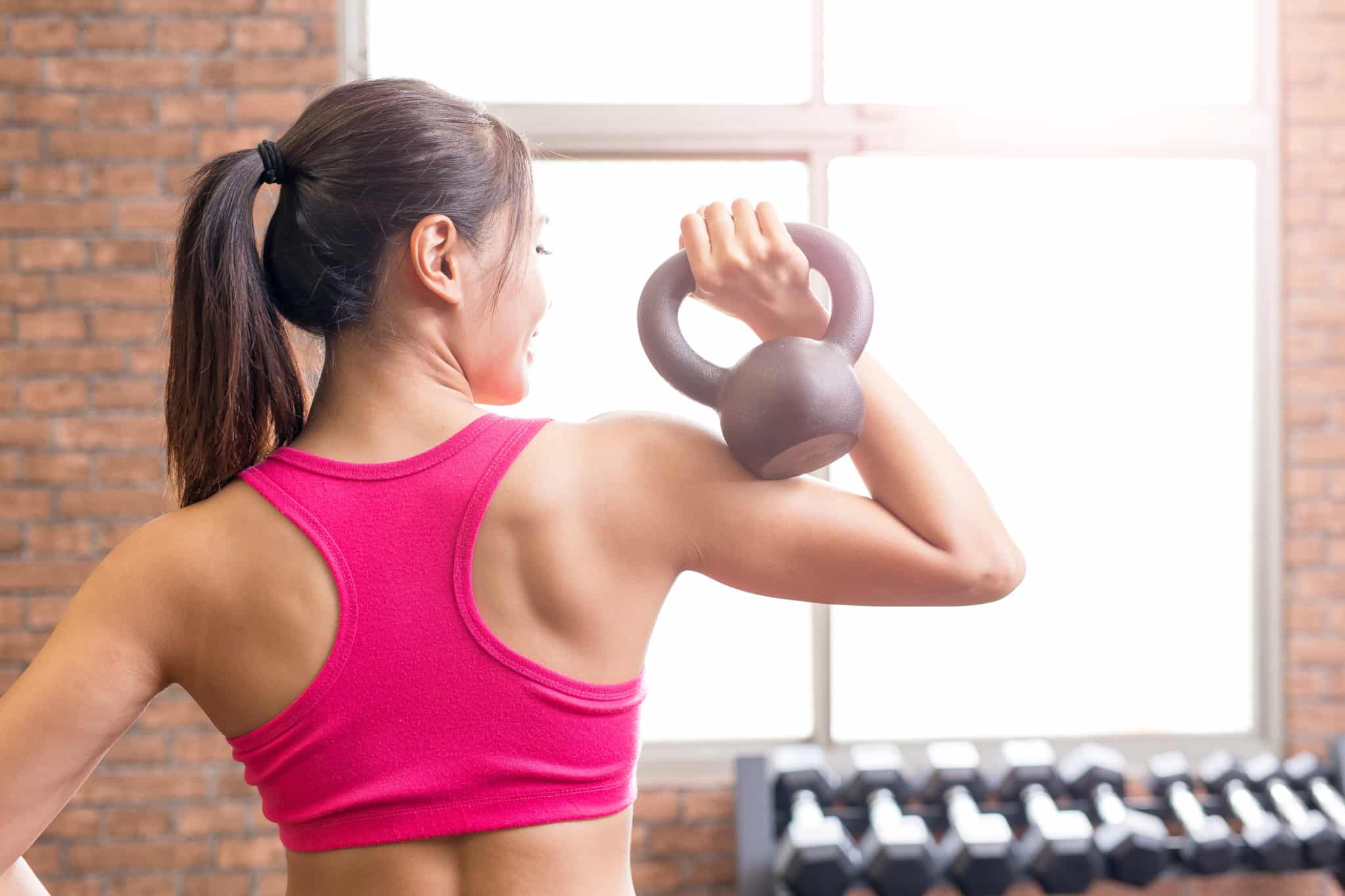 Woman in pink sports bra holding kettlebell over shoulder