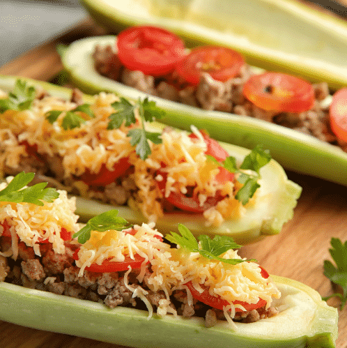 Stuffed zucchini boats with tomatoes and cheese on wood platter