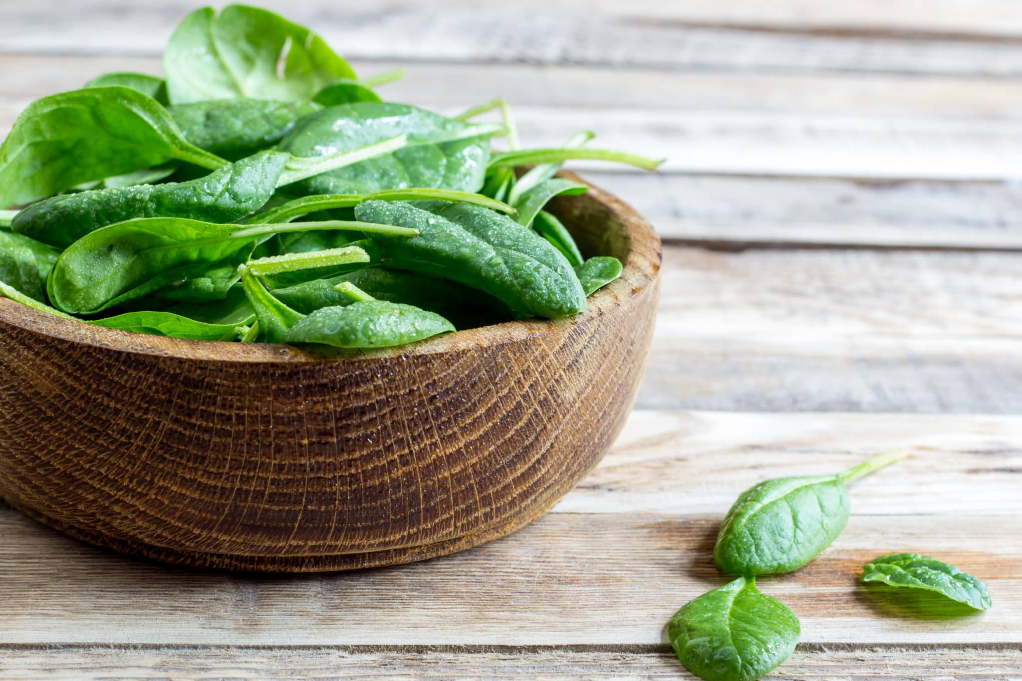 Spinach leaves in bowl on wood table