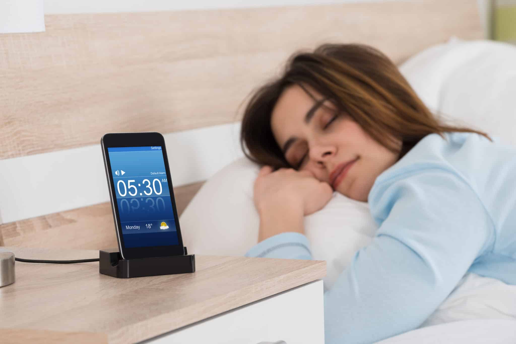 Woman sleeping on pillow with alarm clock set on phone