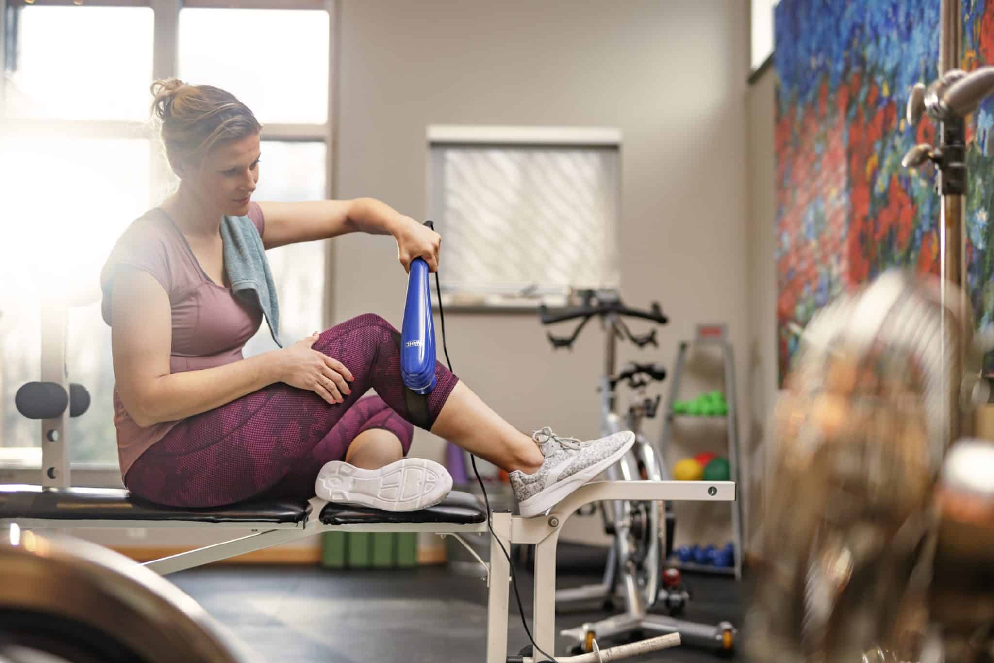 Woman in workout clothes holding Wahl Deep Tissue Massager to leg