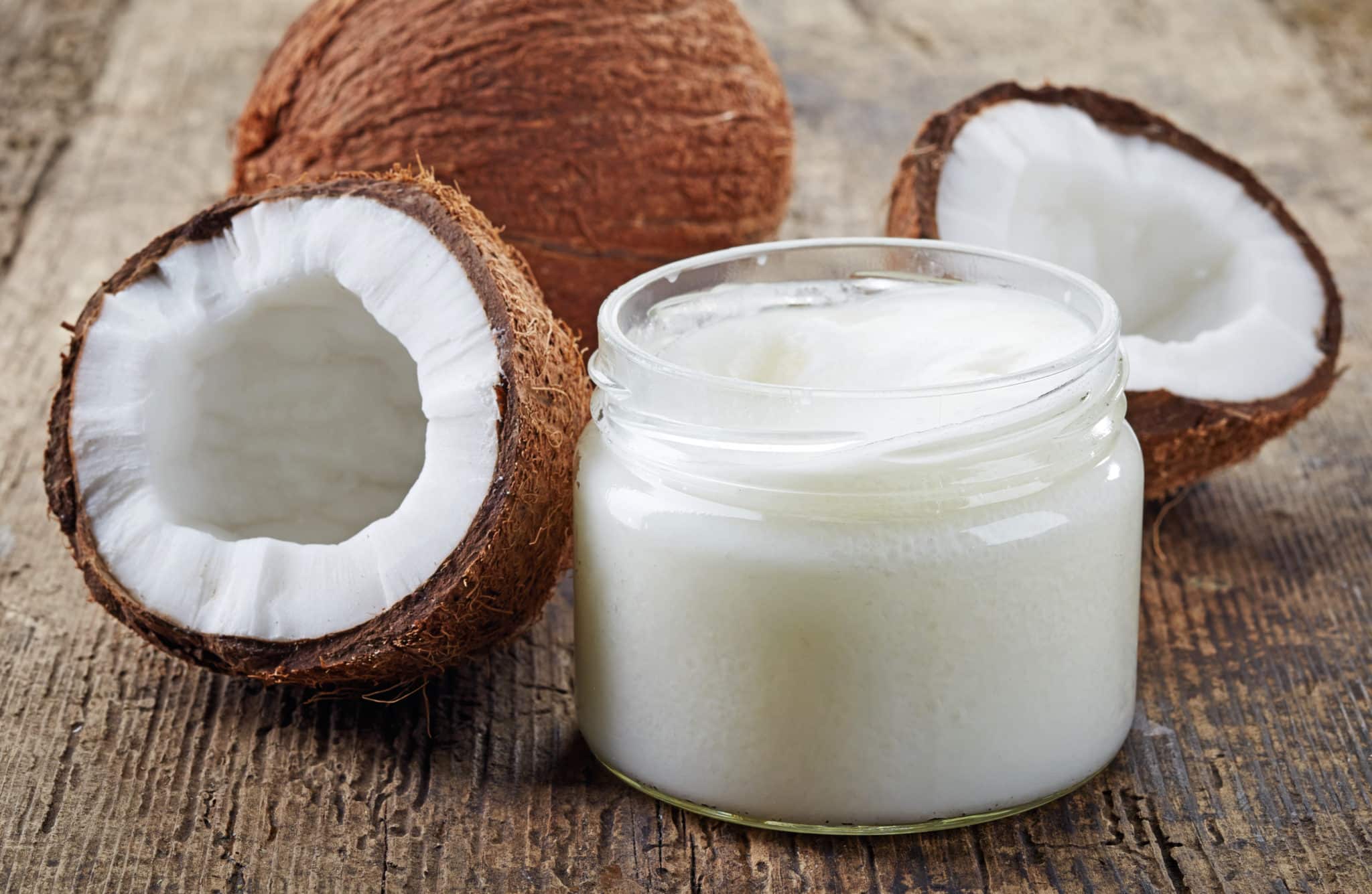 Jar of coconut oil next to whole and halved coconuts